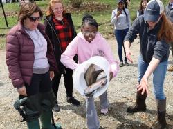 Eleven-year-old Laren Coleman of the South End launches a bucket of hatchery trout during the April 27 fish stocking event at Jamaica Pond hosted by Governor Maura Healey and Boston Parks Commissioner Ryan Woods. The youngster was part of a bucket brigade that transported 1,000 trout down to the water at the spring fish stocking. The state provides the fish for the pond overseen by the Boston Parks and Recreation Department. Photo by Jon Seamans.